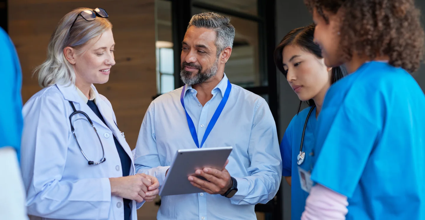 Three healthcare workers stand around another worker holding a tablet
