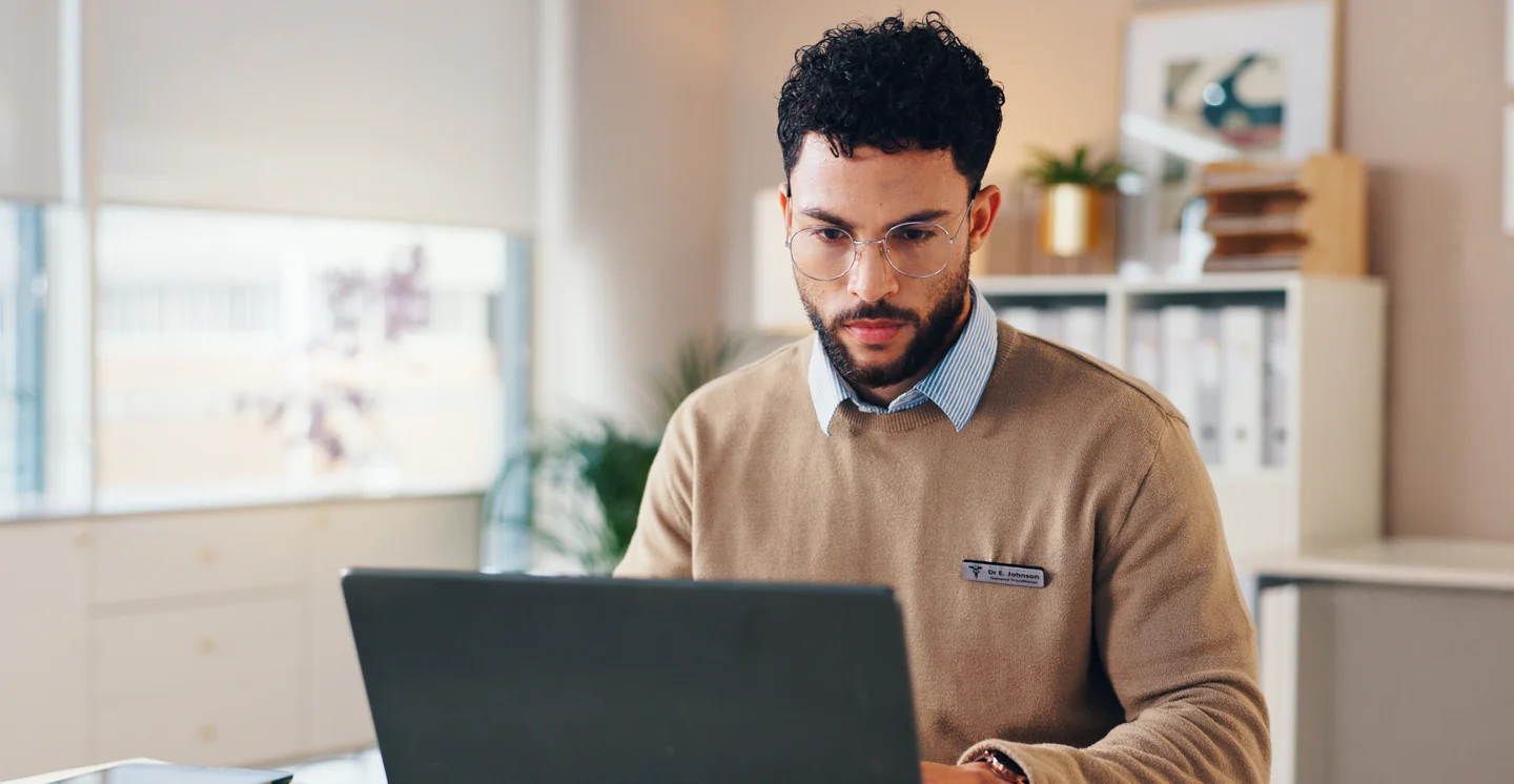 Healthcare worker wearing a name tag indicating they are a doctor sits in front of a computer