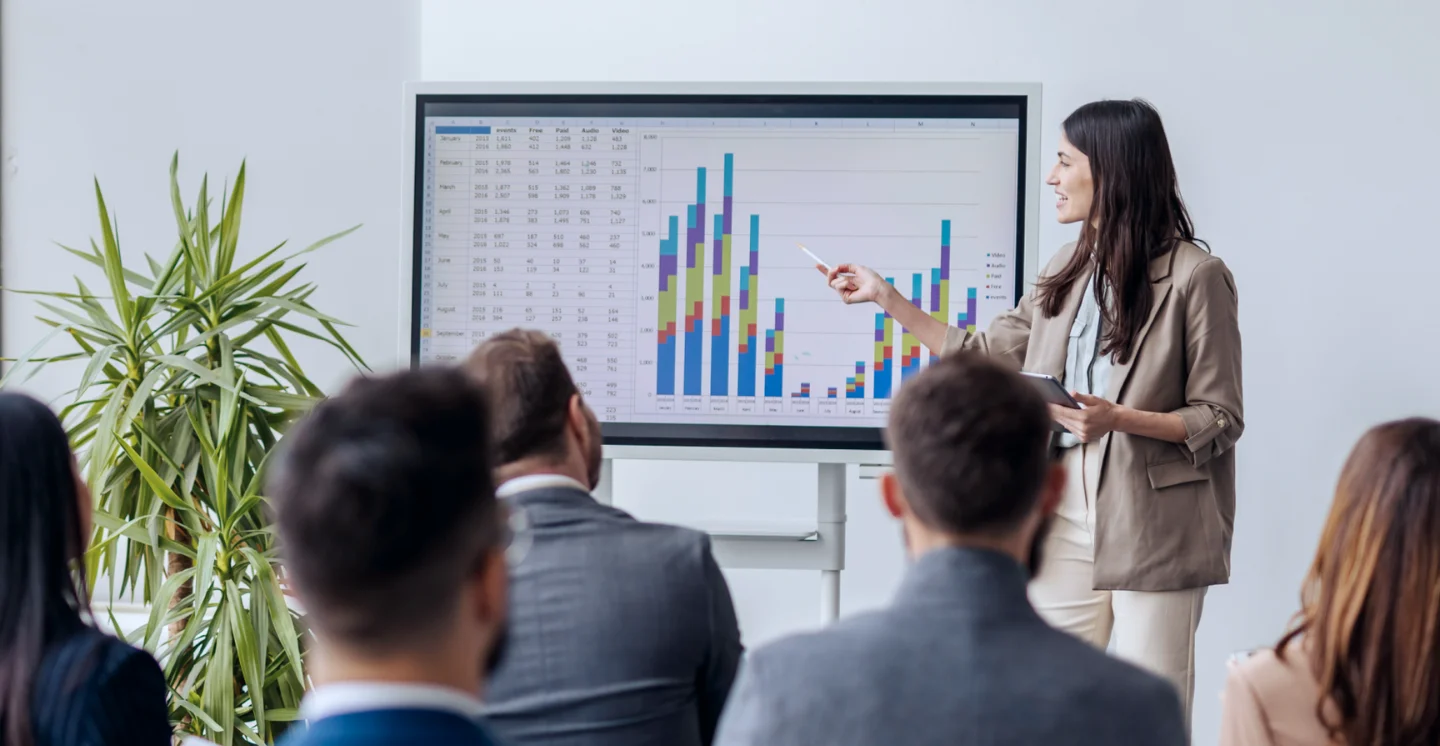 A person stands in front of a chart and explains what's on display to a group of people