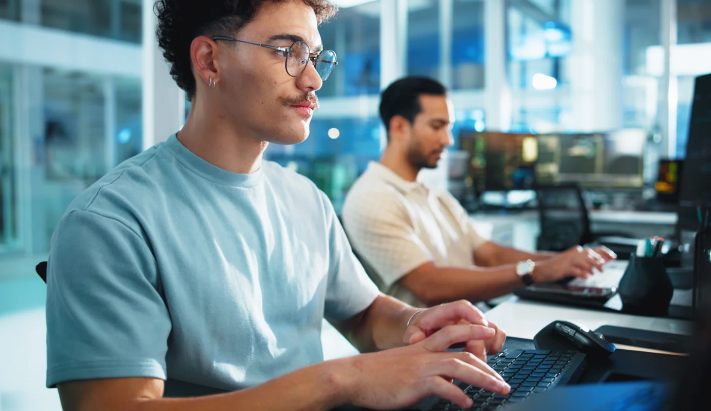Two people sit side-by-side working at computers
